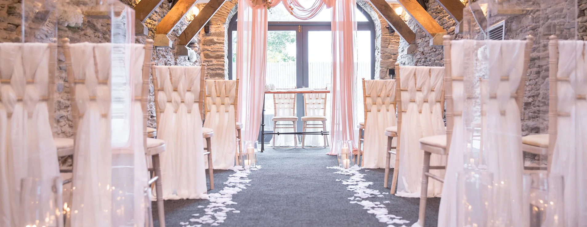 The ceremony room, stone walls and oak beams, set with an aisle of petals